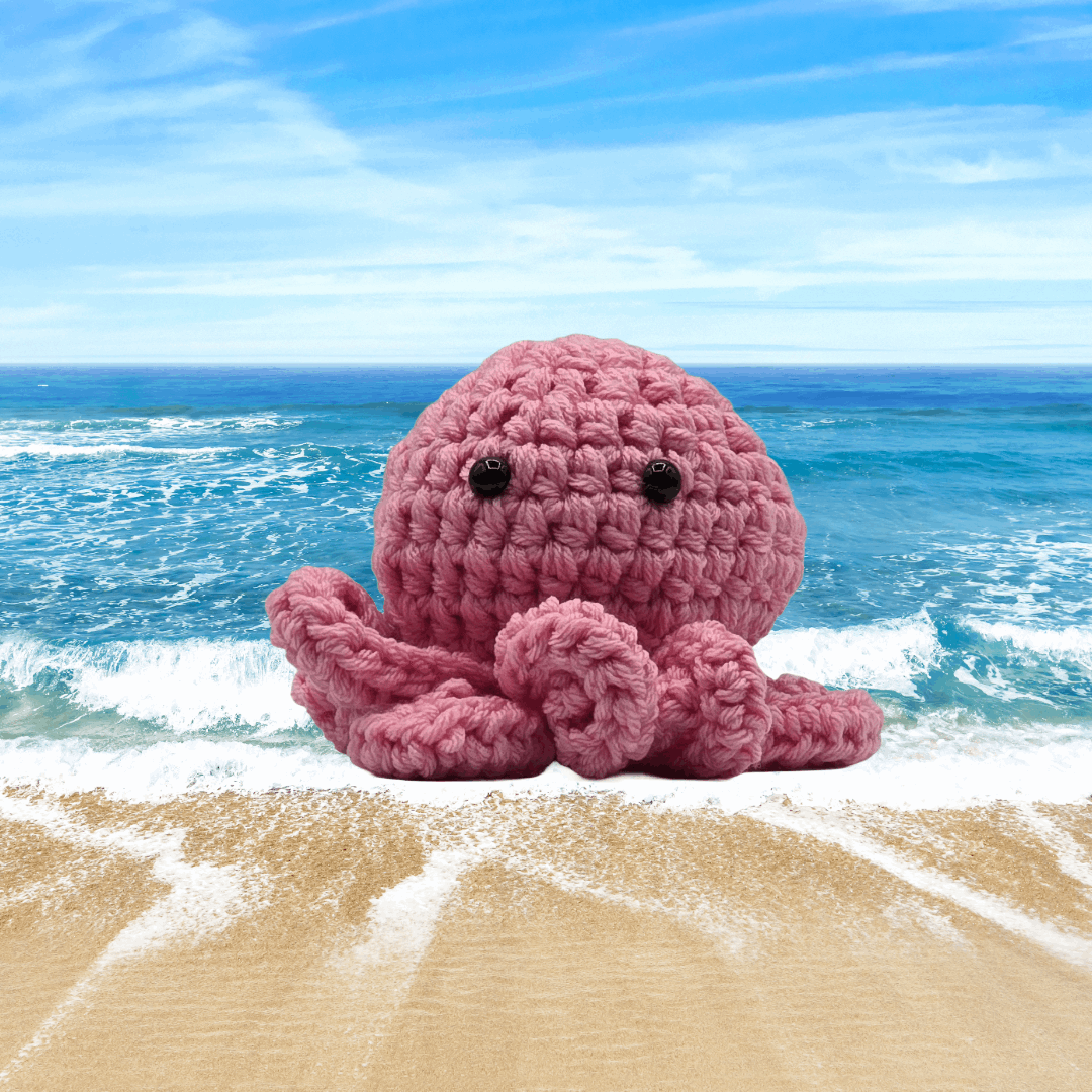 A small crochet octopus sitting by the ocean