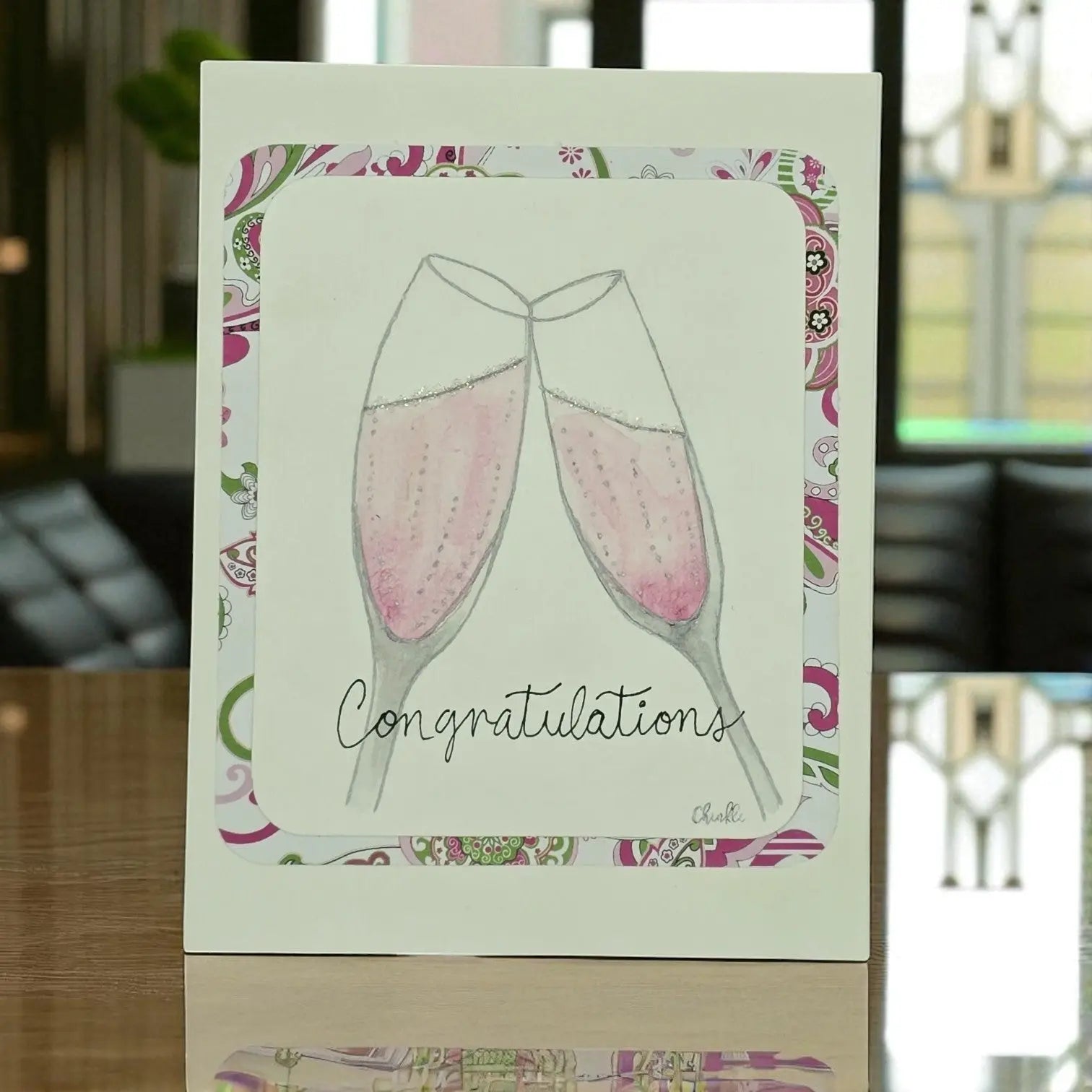 A card adorned with two champagne glasses and the word "Congratulations," featuring a pink wine wedding theme.