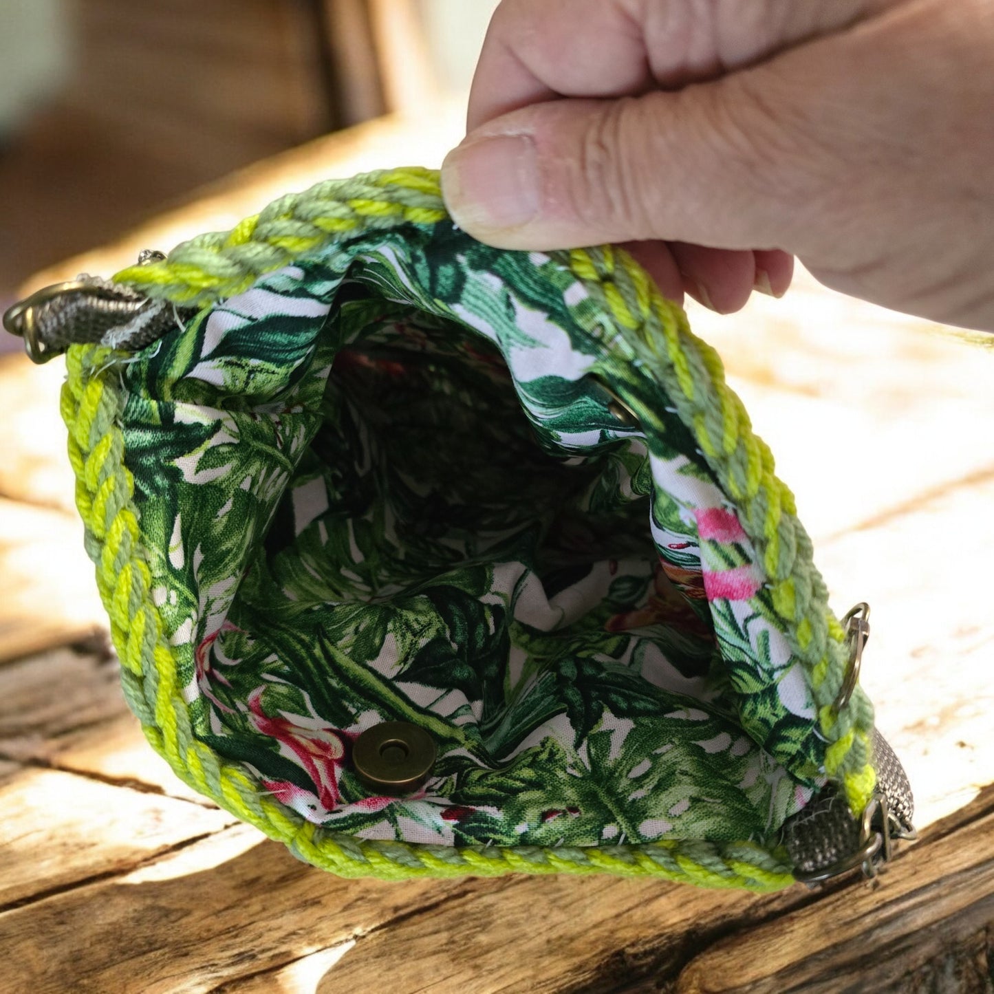 Tropical leaf-patterned fabric inside a green boho crochet bag held by a hand.