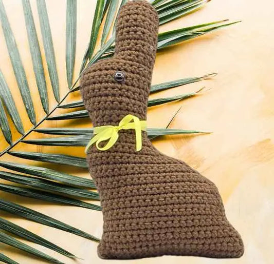 A crocheted chocolate bunny adorned with a yellow ribbon, showcasing intricate stitching and a cute, playful expression.
