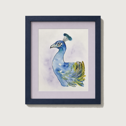 Framed watercolor art print of a blue peacock with green and yellow feather details, set in a dark navy frame with a light lavender mat against a neutral beige wall.