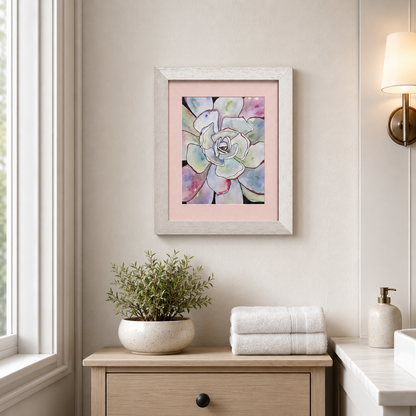 A framed watercolor art print of a succulent flower with pastel colors, displayed on a beige wall above a wooden console table in a styled bathroom setting.