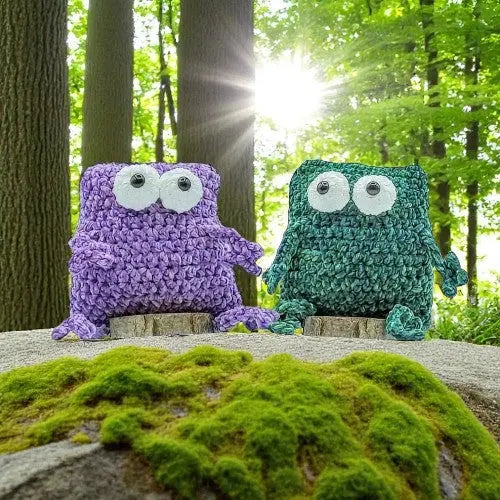 TWO CROCHET FROGS SITTING IN THE FOREST