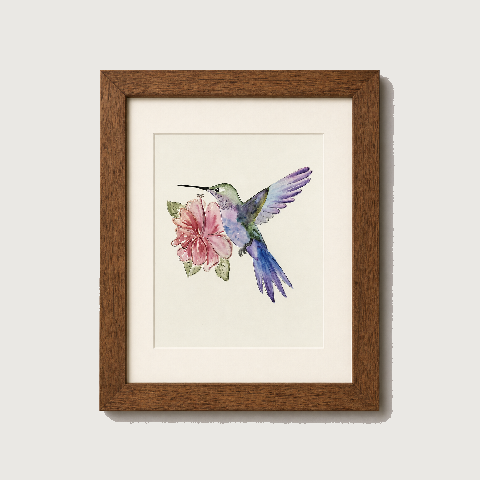 Framed watercolor art print of a hummingbird hovering near a pink flower, set in a brown wooden frame with a white mat against a light gray wall.