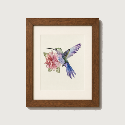 Framed watercolor art print of a hummingbird hovering near a pink flower, set in a brown wooden frame with a white mat against a light gray wall.