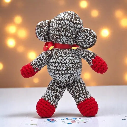 a cute crochet brown and white monkey with red hand feet and ears standing with his back to you