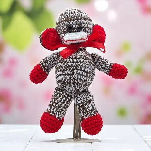 a cute crochet brown and white monkey with red hand feet and ears standing with his facing you