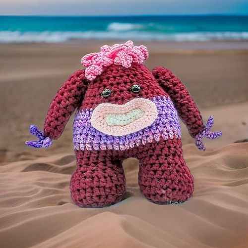 A crocheted stuffed monster toy featuring a purple body with pink hair, showcasing intricate stitching and a playful design.