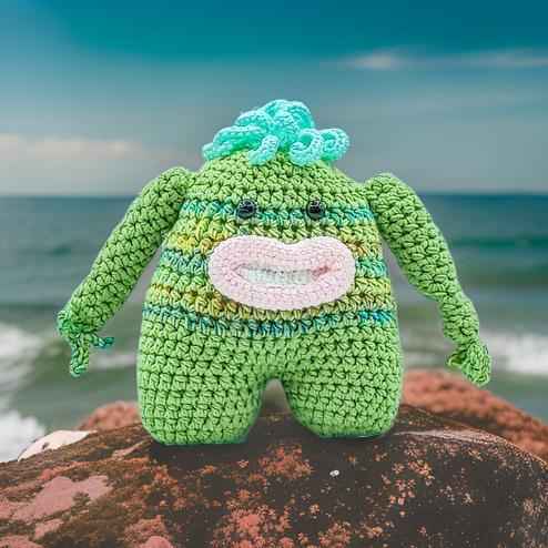 A cheerful green crocheted monster with a wide smile, showcasing its playful and friendly character.