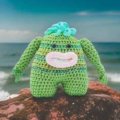 A cheerful green crocheted monster with a wide smile, showcasing its playful and friendly character.