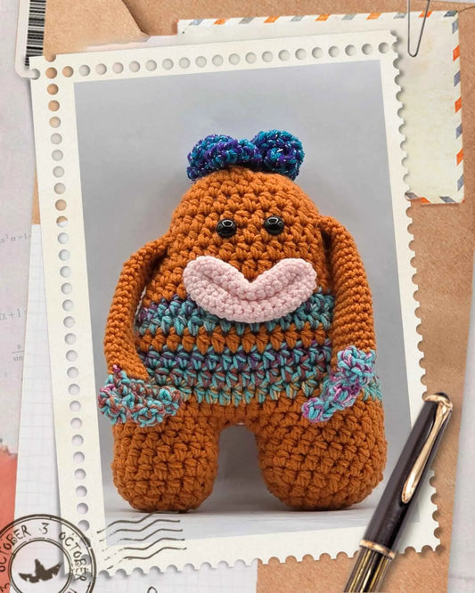 A crocheted toy monster of a whimsical orange and blue hair with large eyes and a playful expression.
