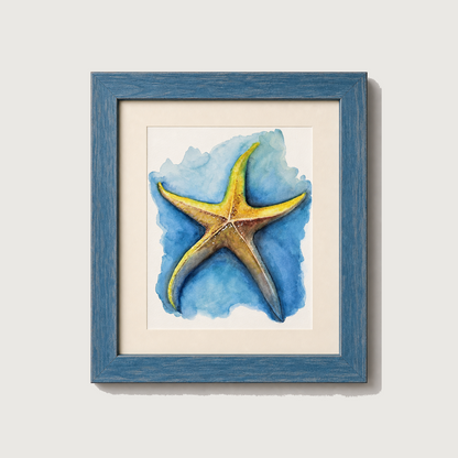 Framed wall art featuring a watercolor-style yellow starfish on a blue watercolor background, set in a distressed blue frame with a white mat against a light gray wall.