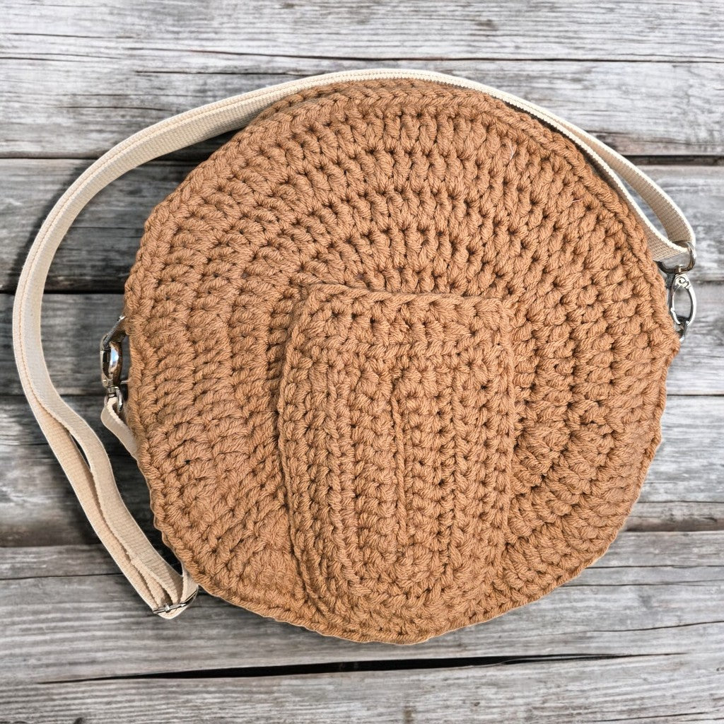 Round boho crochet bag with a beige strap on a wooden surface