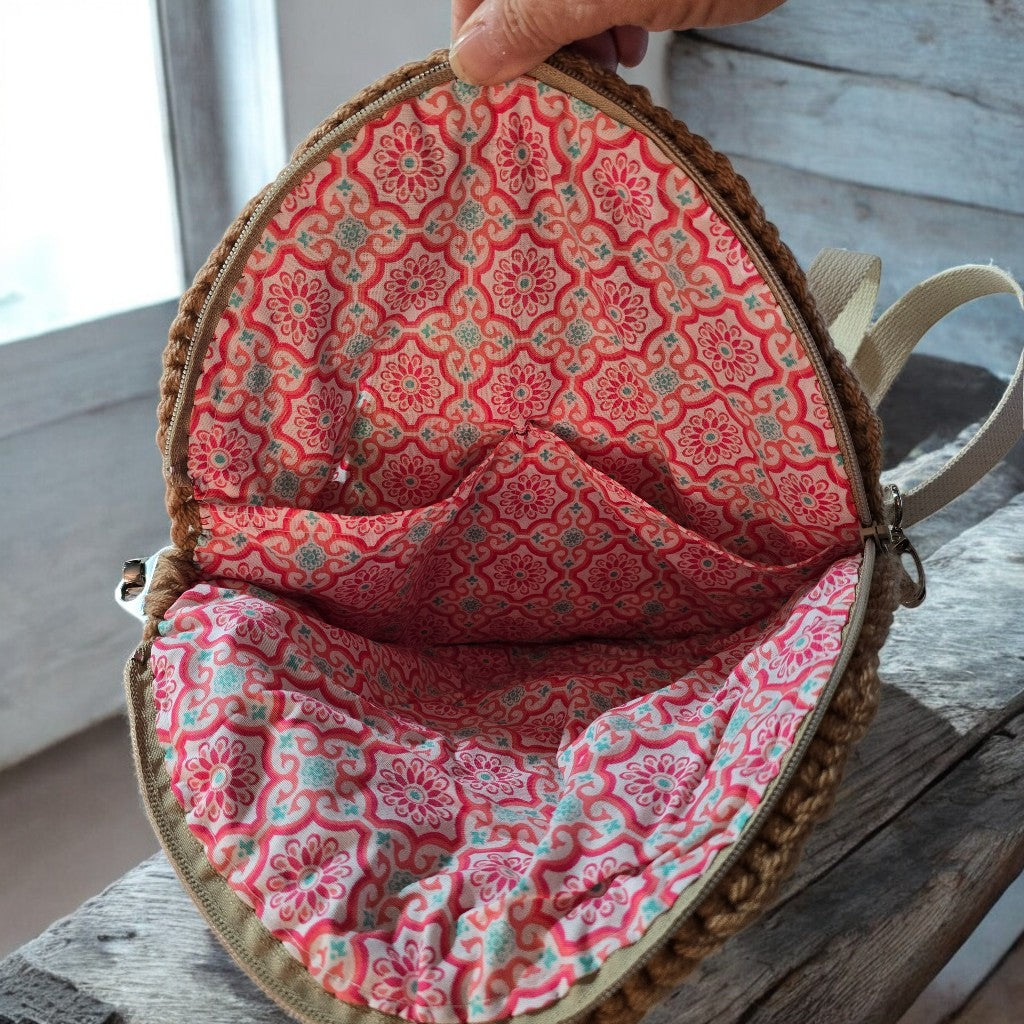 Inside pouch of a boho crochet bag with pink floral pattern held by a hand on a wooden surface.