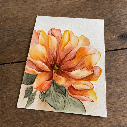 A square watercolor painting of a large orange and yellow flower with green leaves on textured white paper, placed on a dark brown wooden surface.