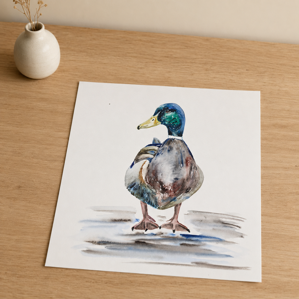 A square art print featuring a watercolor painting of a mallard duck standing on a light wood surface next to a small white ceramic vase.
