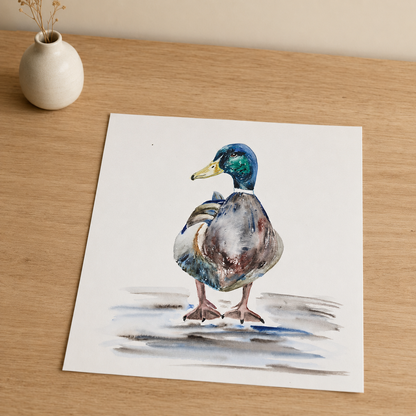 A square art print featuring a watercolor painting of a mallard duck standing on a light wood surface next to a small white ceramic vase.