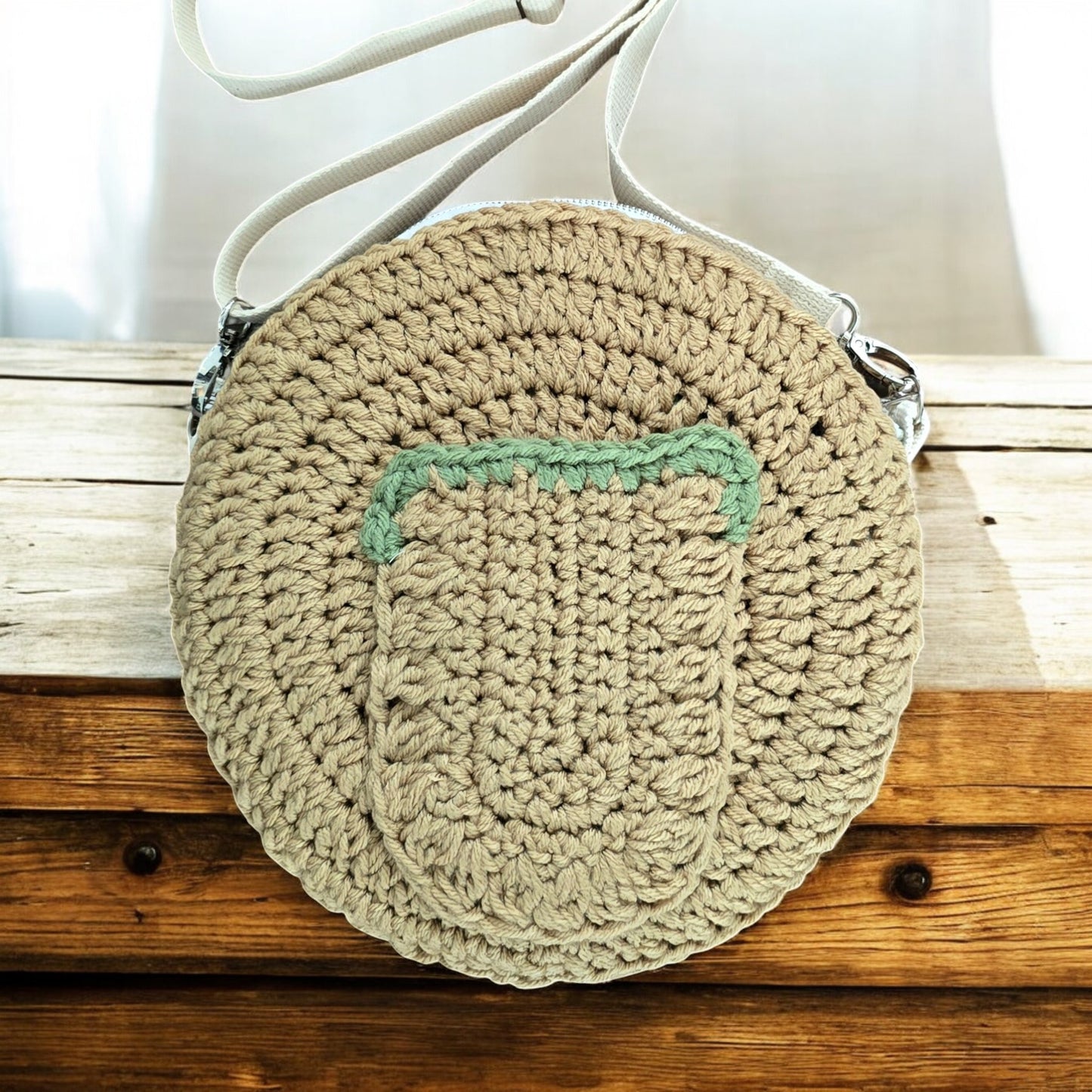 Round boho crochet bag with a green pocket on a wooden surface